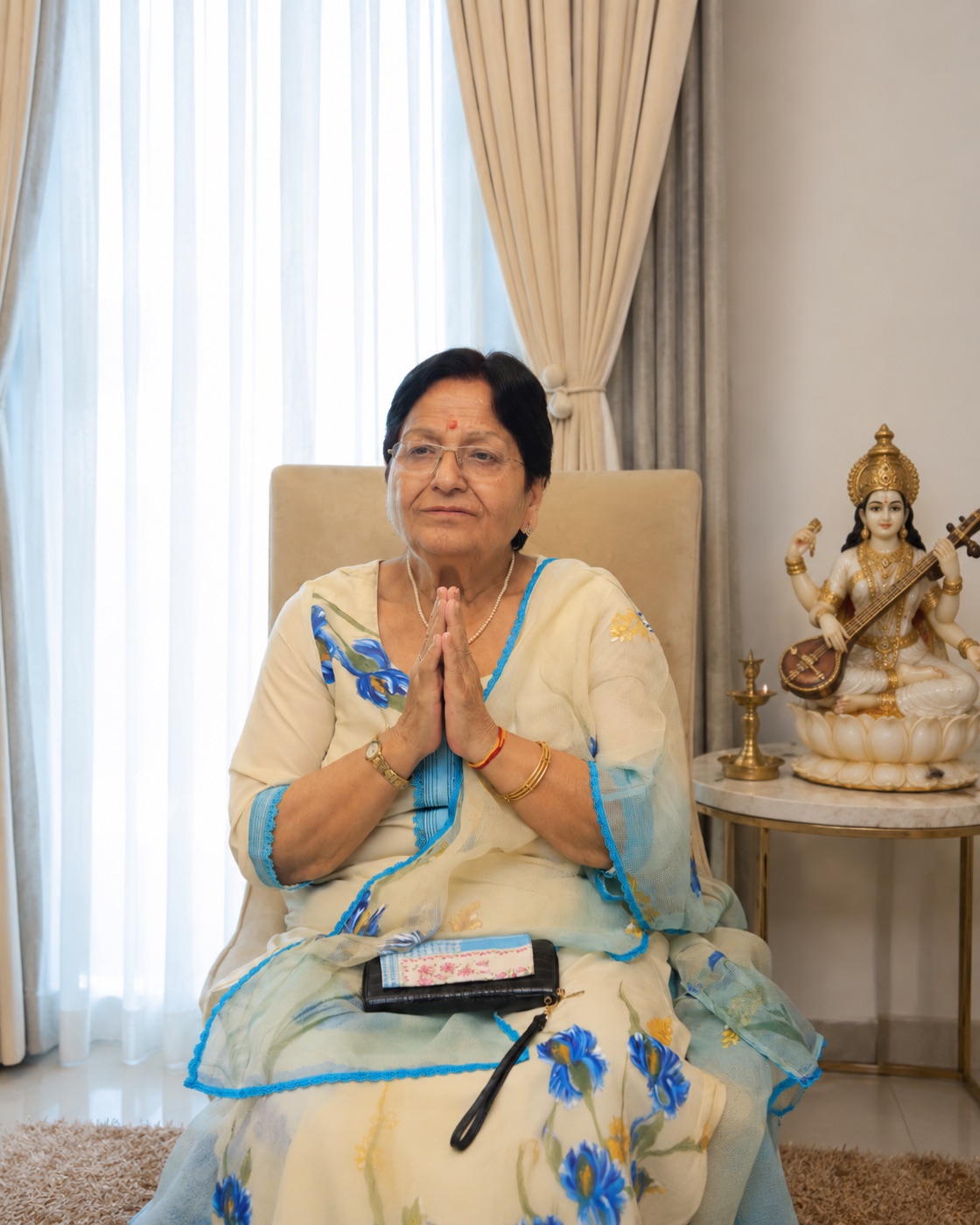 Smt. Parveen Chopra greeting with folded hands, beside a Saraswati idol